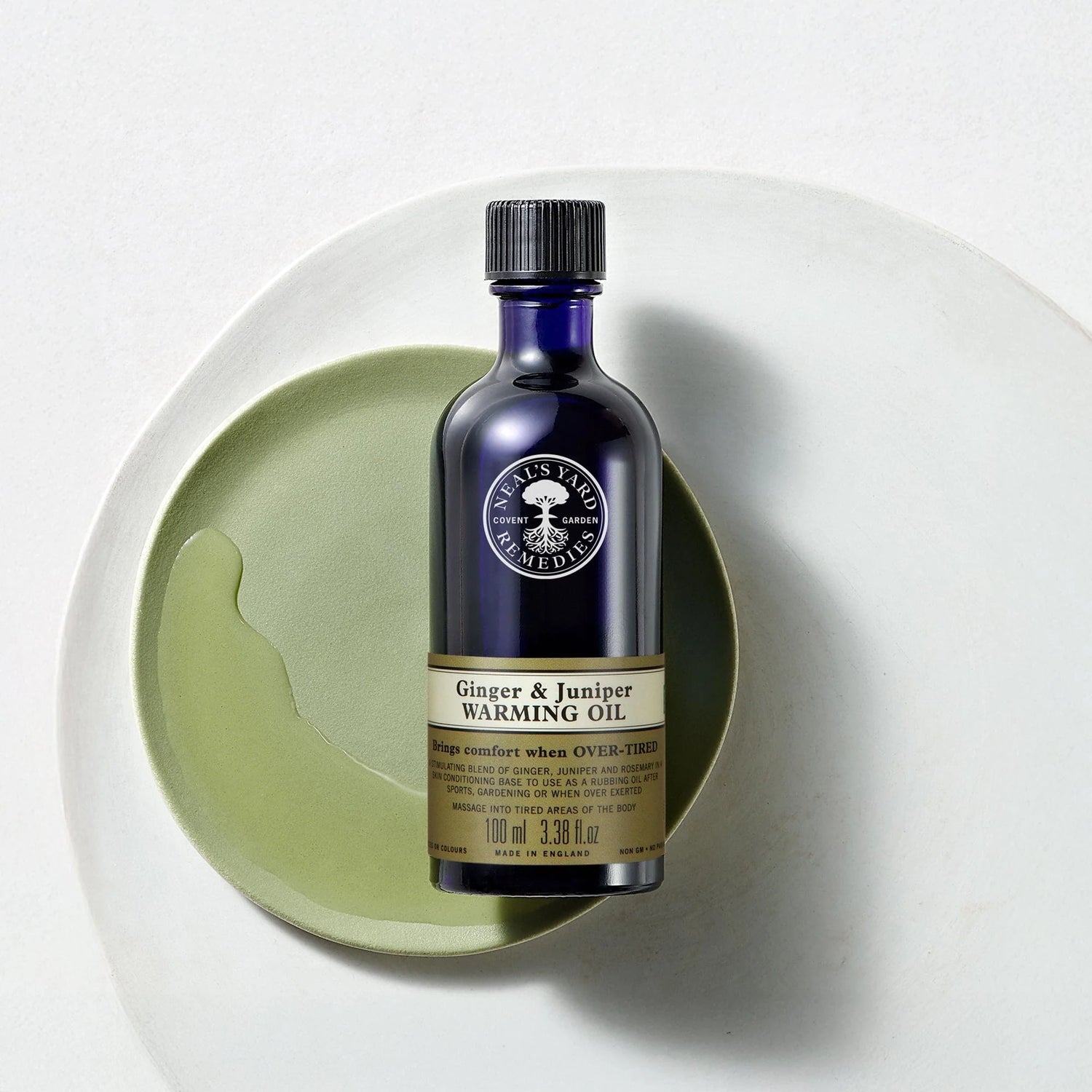 Bottle of 'Ginger & Juniper Warming Oil' on a white plate with a light green background